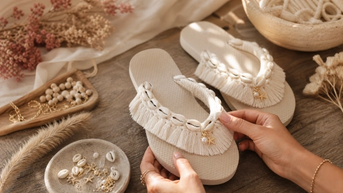 Finished sandals trimmed with cowrie shells and fringe on a wooden table