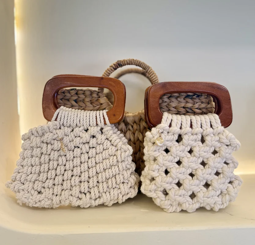 Two small macrame bags with rectangular wooden handles and shell charms, side by side on a studio shelf in Bali